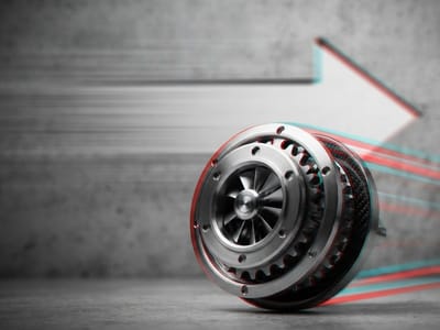 A metallic mechanical turbine component rolling forward against a textured concrete wall with a large directional arrow and motion blur lines.