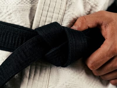 Hand gripping the knot of a black belt on a white martial arts uniform