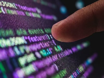 Fingertip touching a screen filled with lines of purple and green programming code