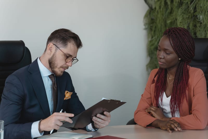 Two people in a job interview at a modern office table beside floor-to-ceiling windows